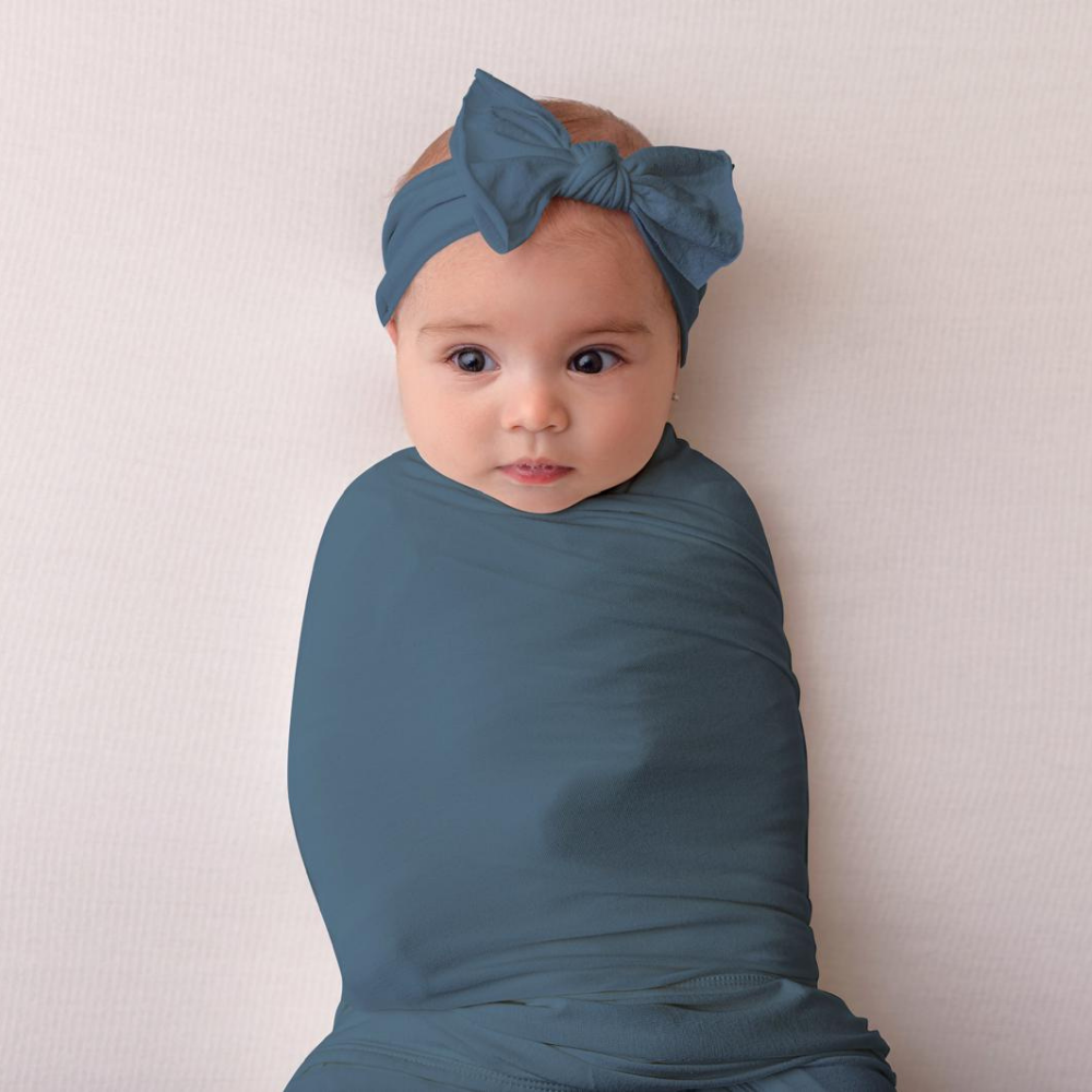 Baby wrapped in a blue blanket with a matching headband against a plain background