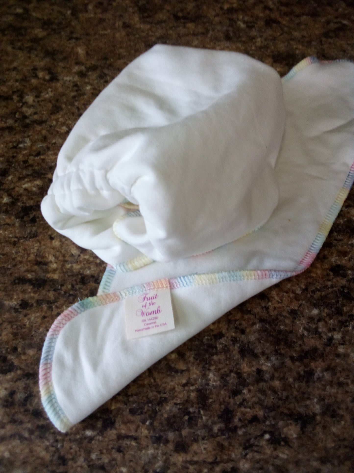 White baby hat with colorful trim on a brown surface