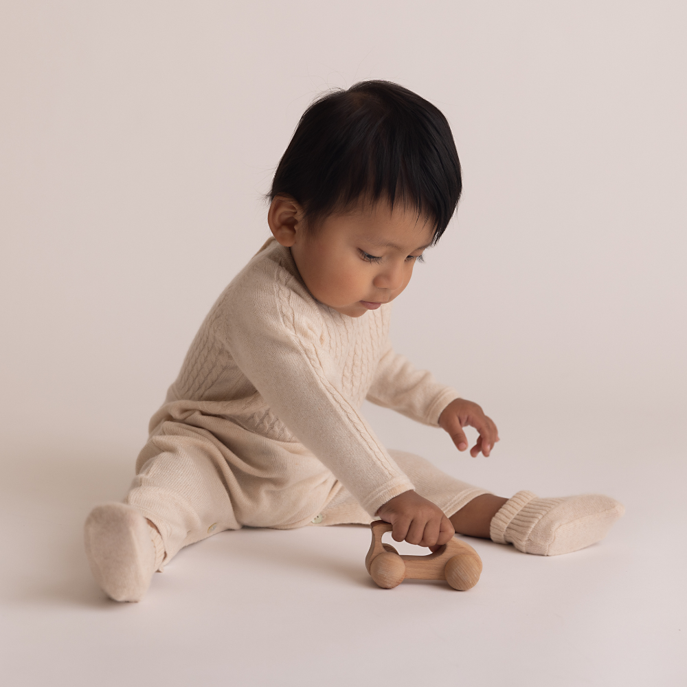 Child in a beige outfit playing with a wooden toy on a light background