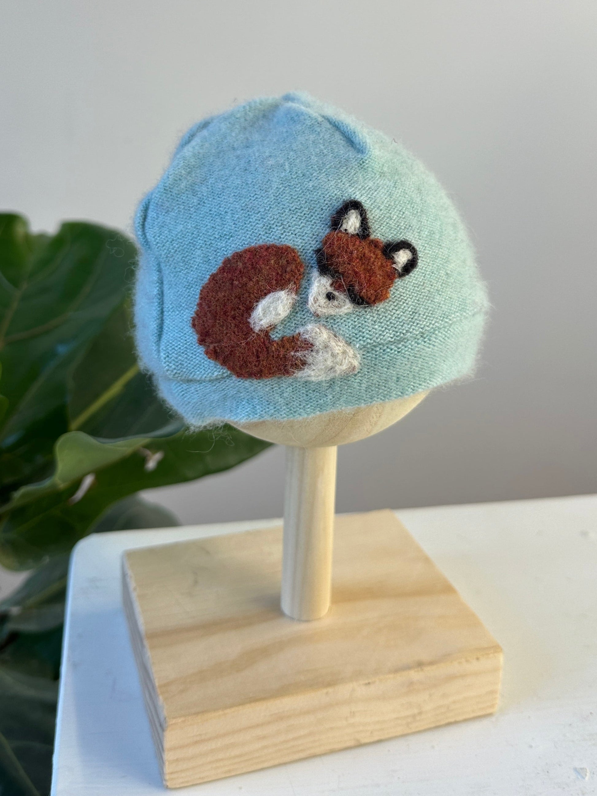 Knitted hat with a fox design on a wooden stand against a neutral background
