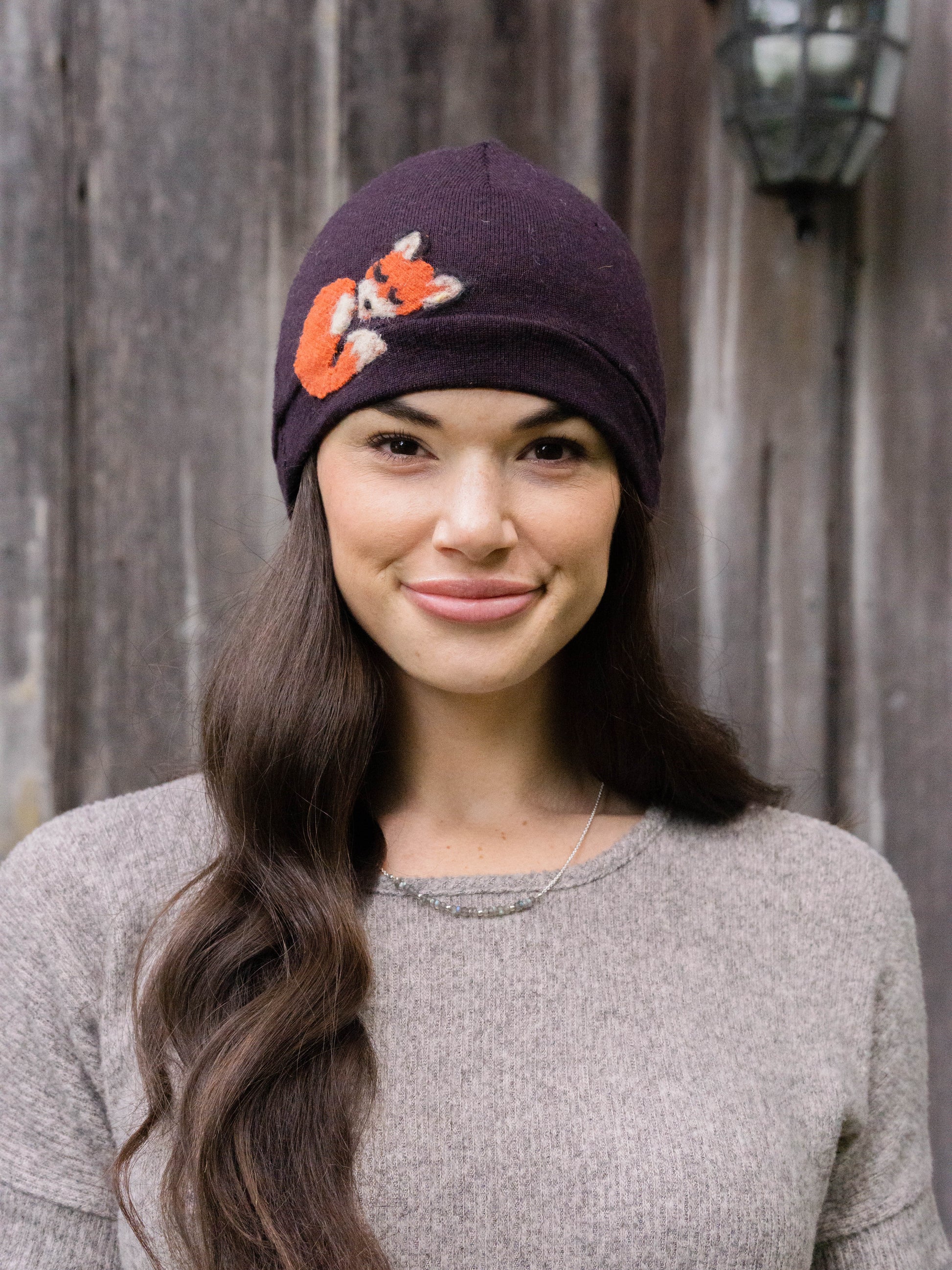 Woman wearing a dark purple beanie with a fox design outdoors.