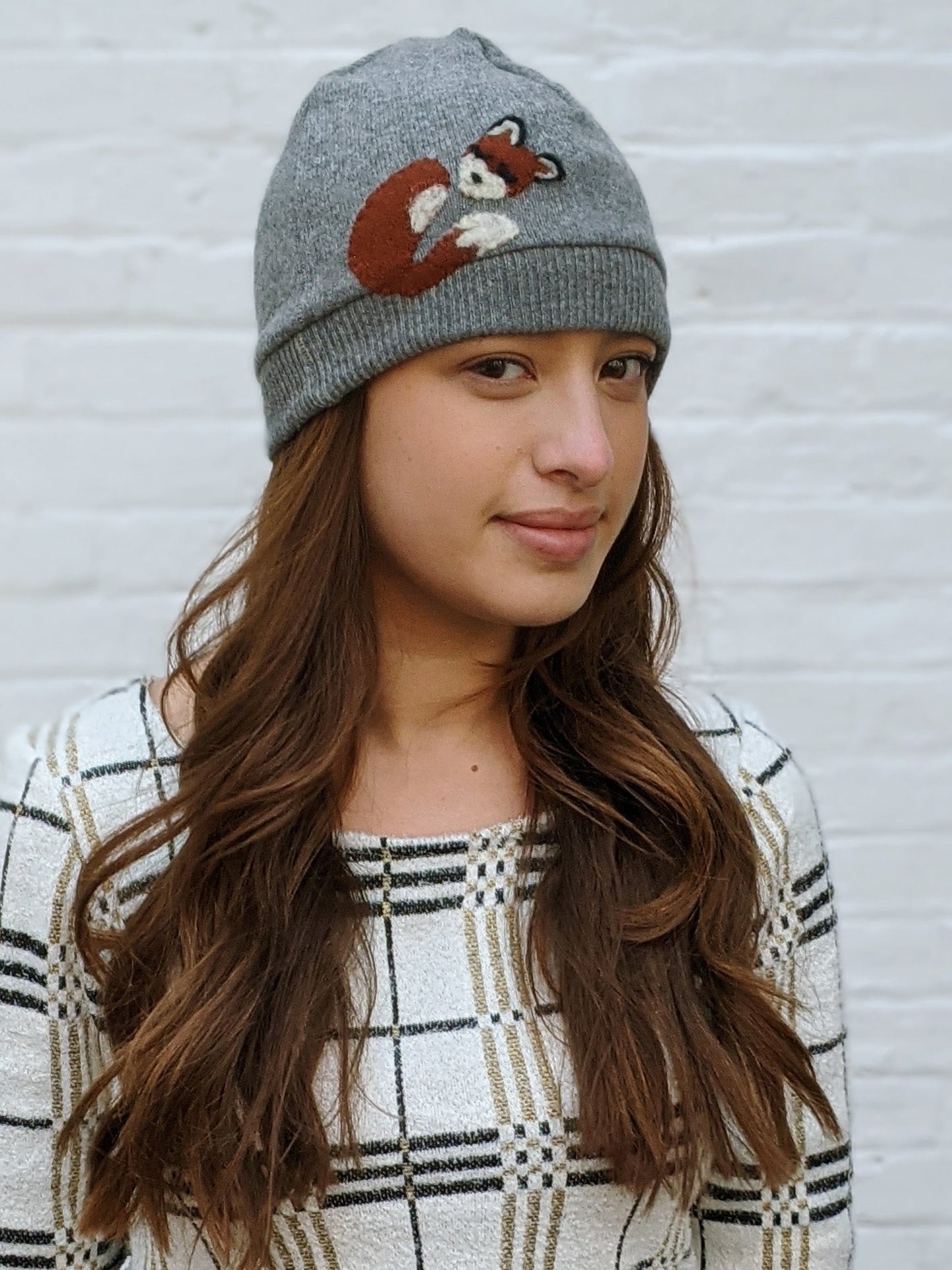 Woman wearing a gray beanie with a fox design against a white background