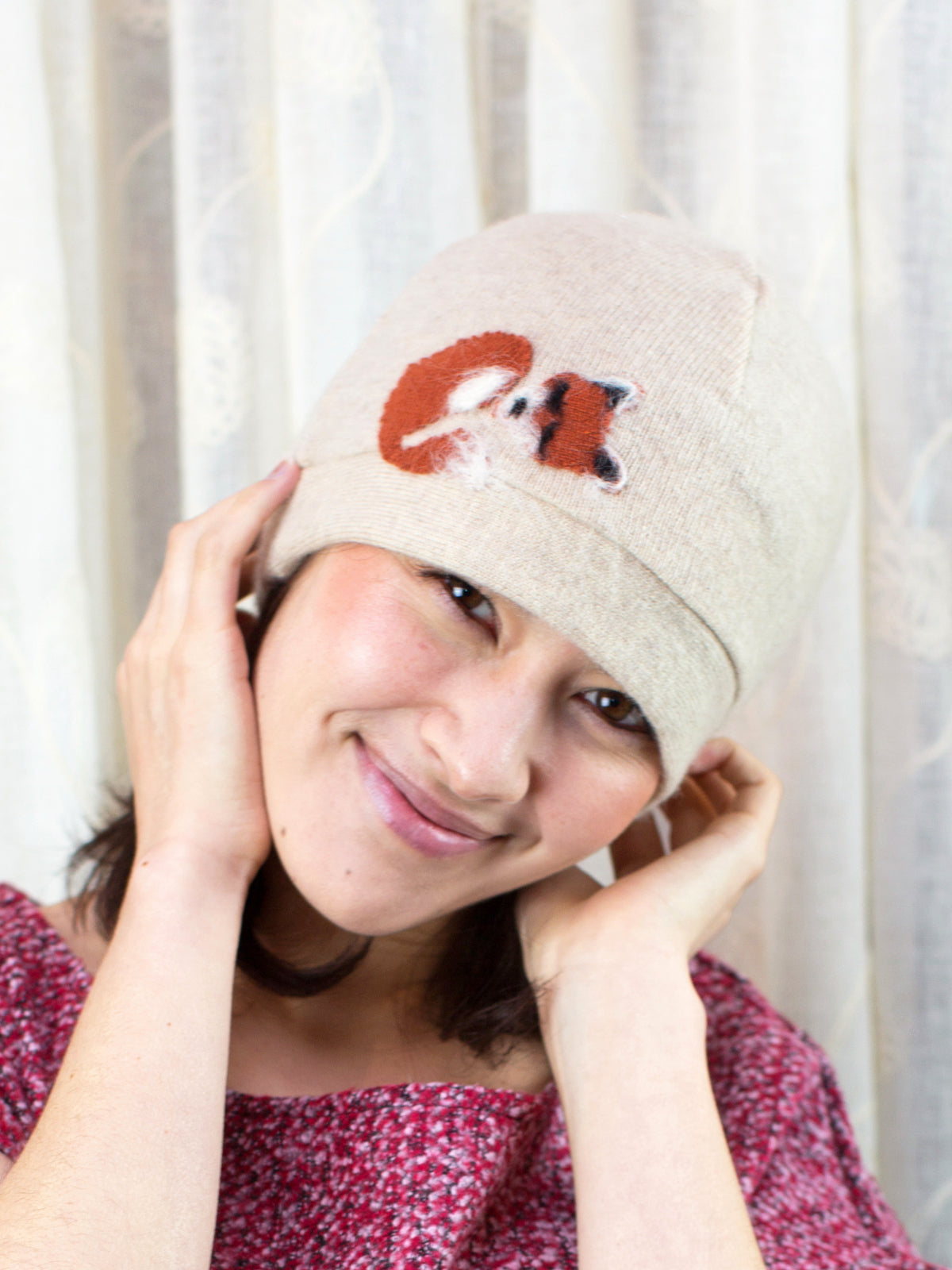 Person wearing a beige beanie with a fox design against a white curtain background