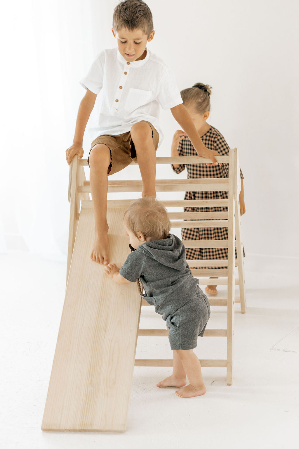 Three children playing on a set of wooden chairs against a white background