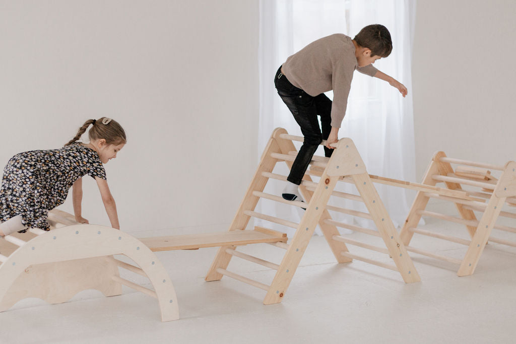 Two children playing on a wooden climbing structure in a bright room.