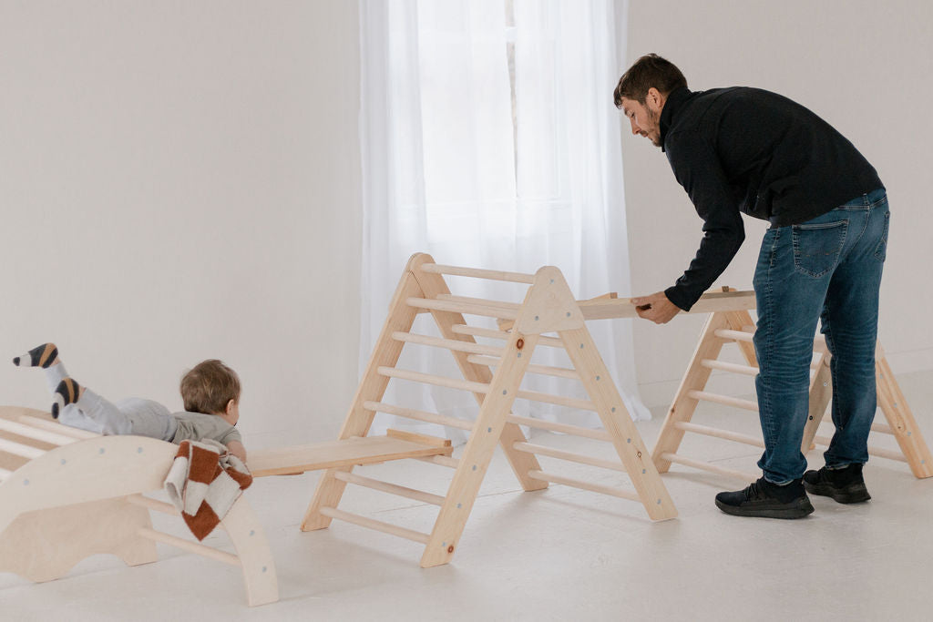Man and child playing with wooden climbing structures in a minimalistic room.