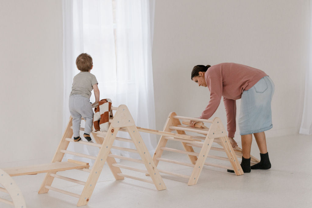 Woman and child playing with wooden climbing structures in a bright room