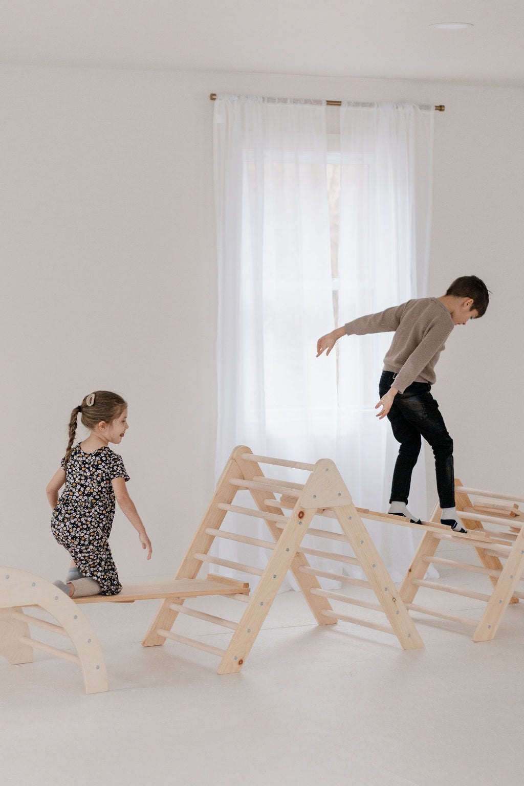 Two children playing with a wooden climbing structure in a minimalistic room.