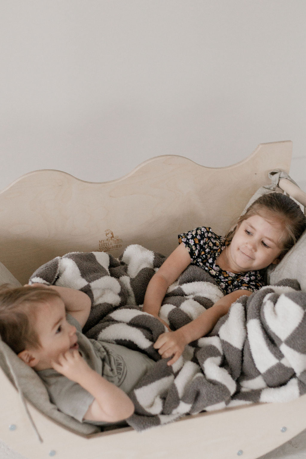 Two children lying on a bed with a gray and white checkered blanket.