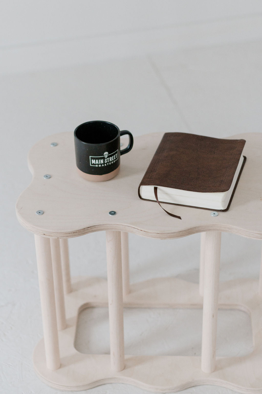 Small wooden table with a black mug and brown notebook on a light background