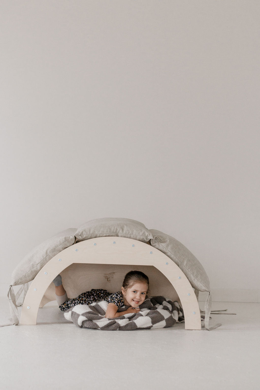 Child playing inside a modern children's playhouse with a gray cushion on a white background