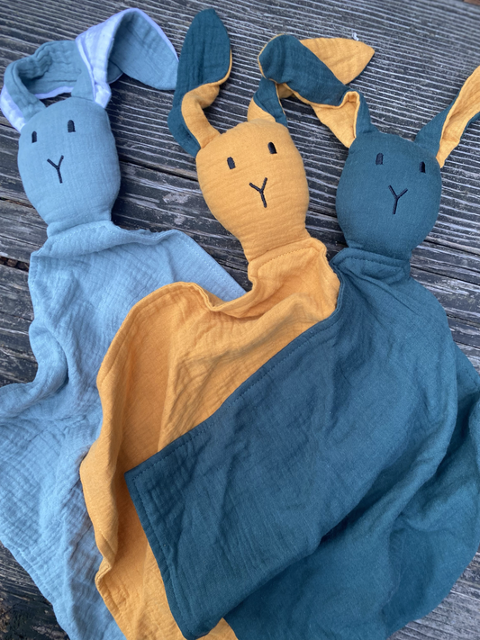 Three soft toy figures in blue, yellow, and teal on a textured surface