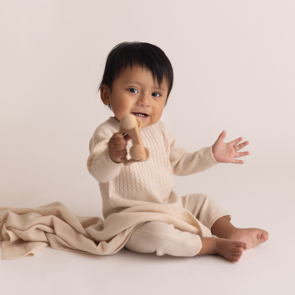 Baby in a natural romper holding a wooden toy on a plain background