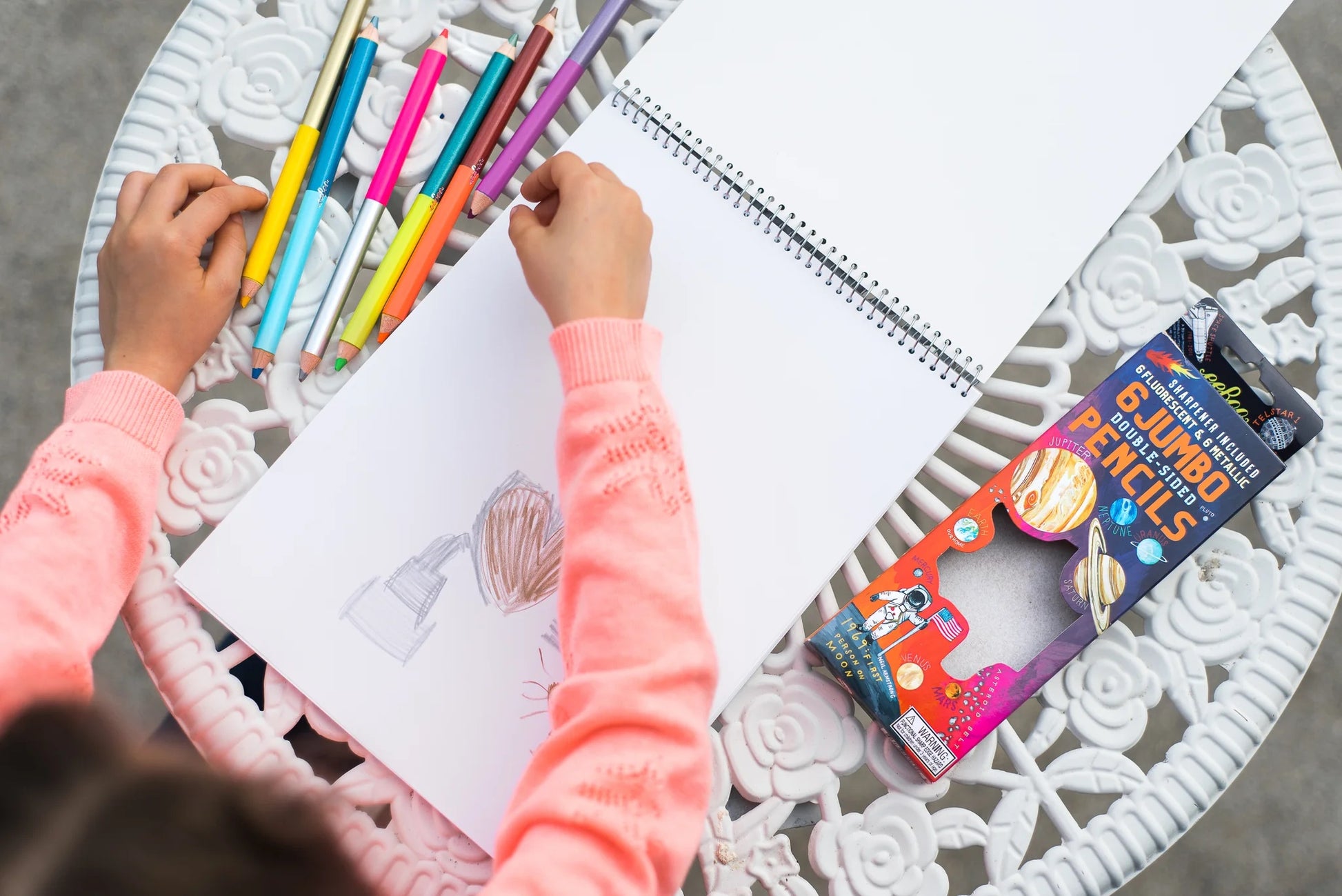 child wearing a pink sweater drawing with Solar System Double-Sided Jumbo Pencils on a sketchbook