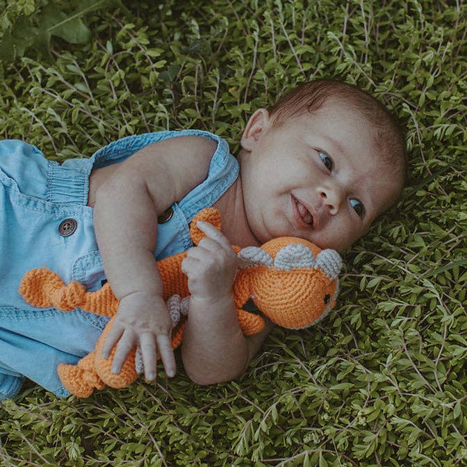 Baby lying on grass with a toy, wearing blue overalls