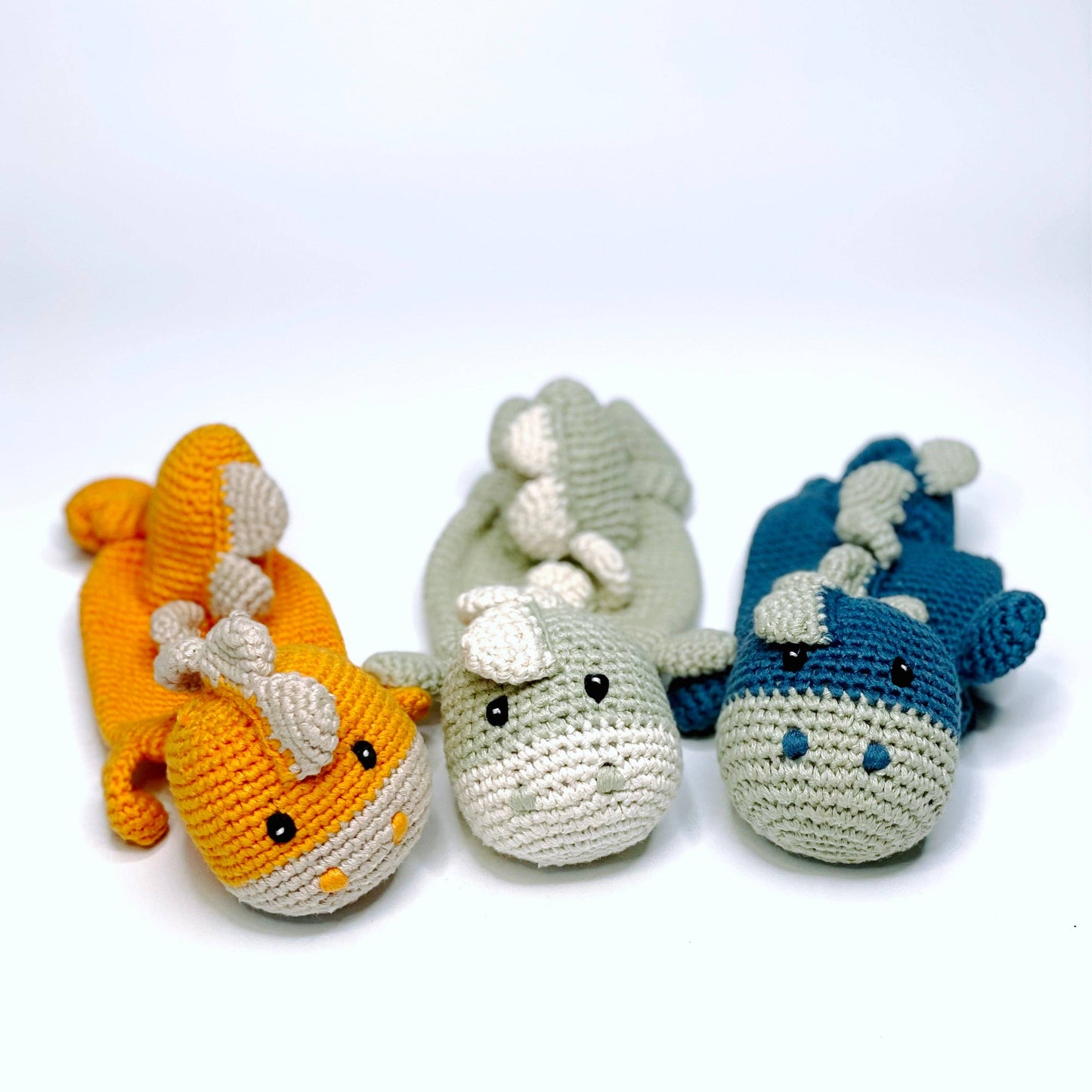 Three crocheted shark toys in orange, gray, and blue on a white background