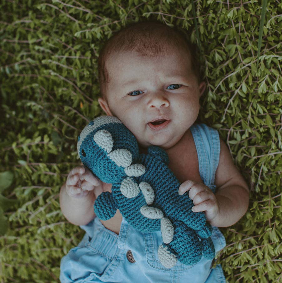 Baby holding a blue dinosaur toy on a grassy background