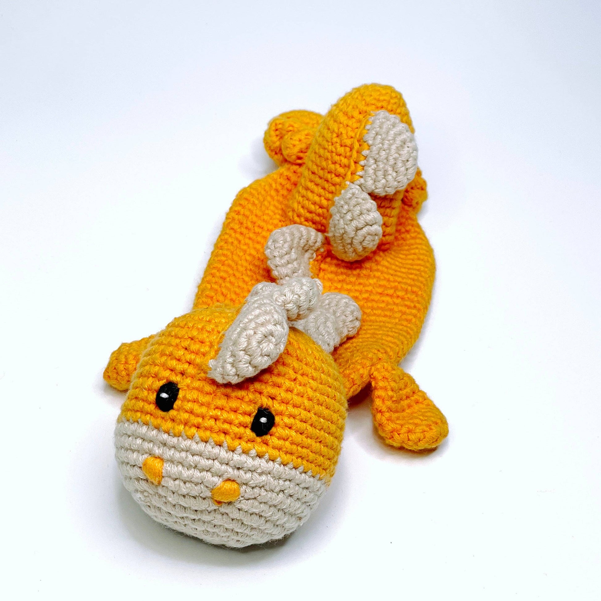 Crocheted toy resembling a fish with orange body and white fins on a white background