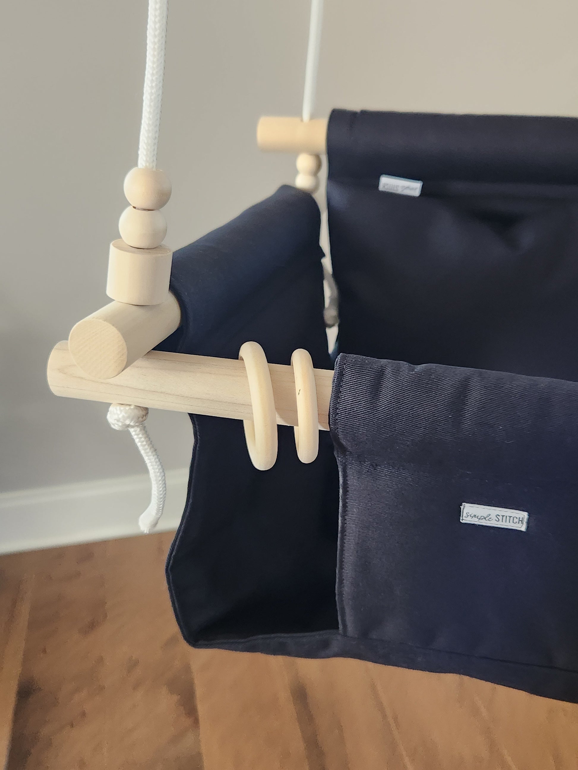 Navy blue baby swing with wooden components against a neutral wall.