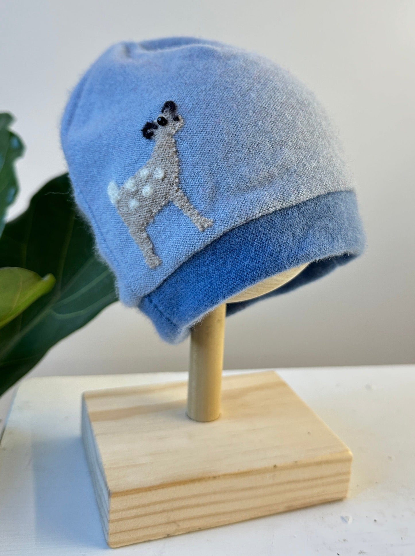 Blue beanie with a dog design on a wooden stand against a white background