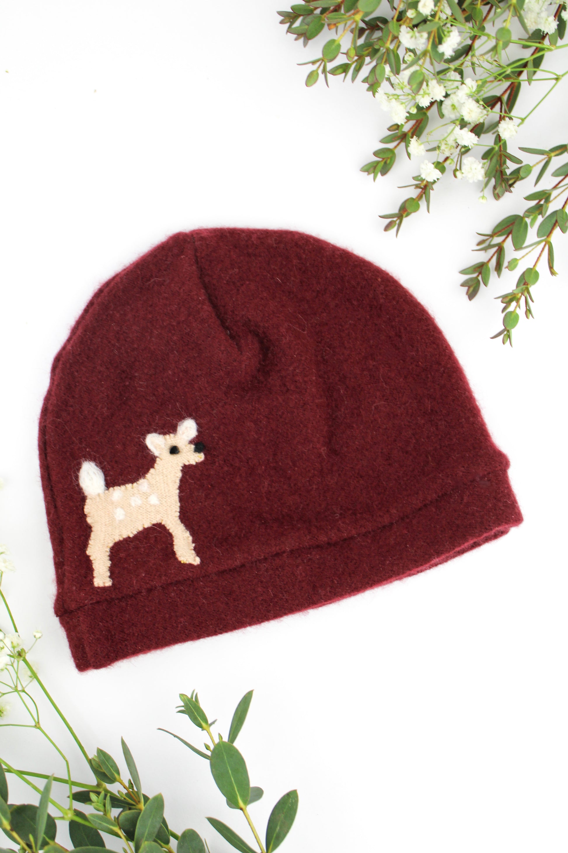 Maroon baby hat with a small dog design on a white background with green leaves.