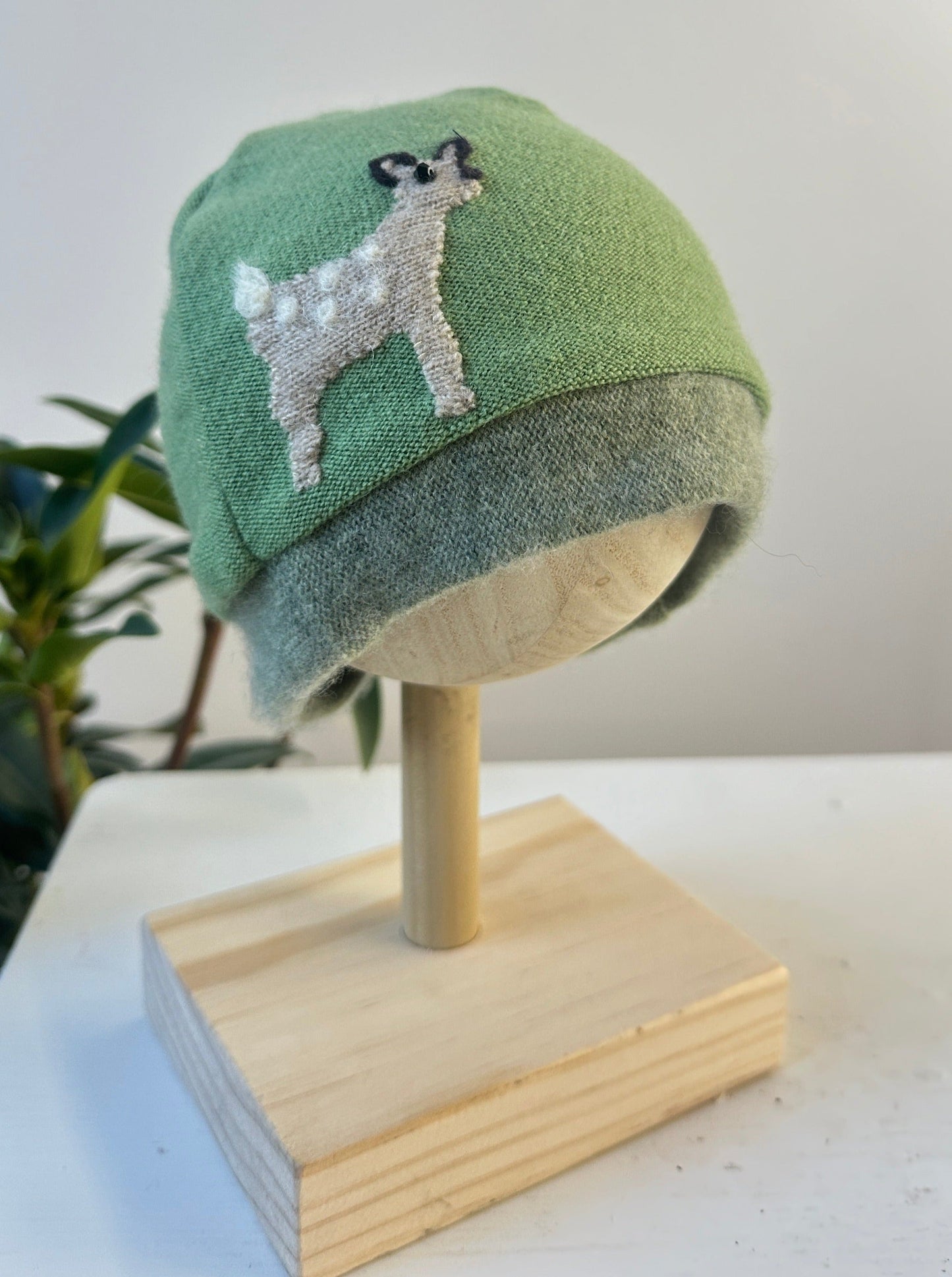 Green beanie with a dog design on a wooden mannequin head against a white background