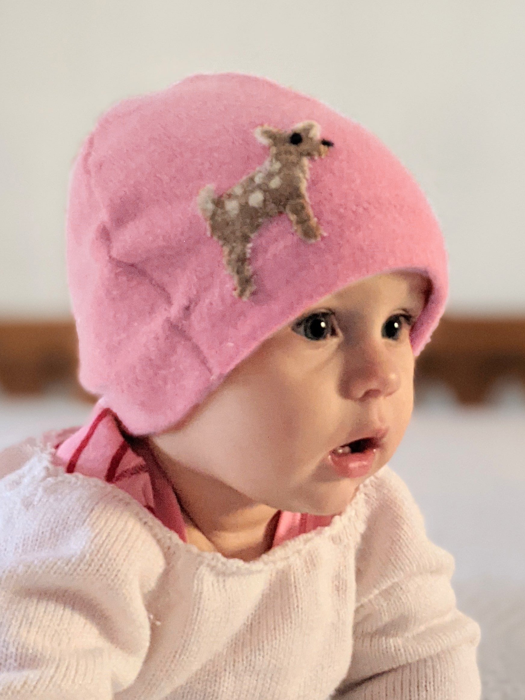 Baby wearing a pink hat with a deer design on a neutral background