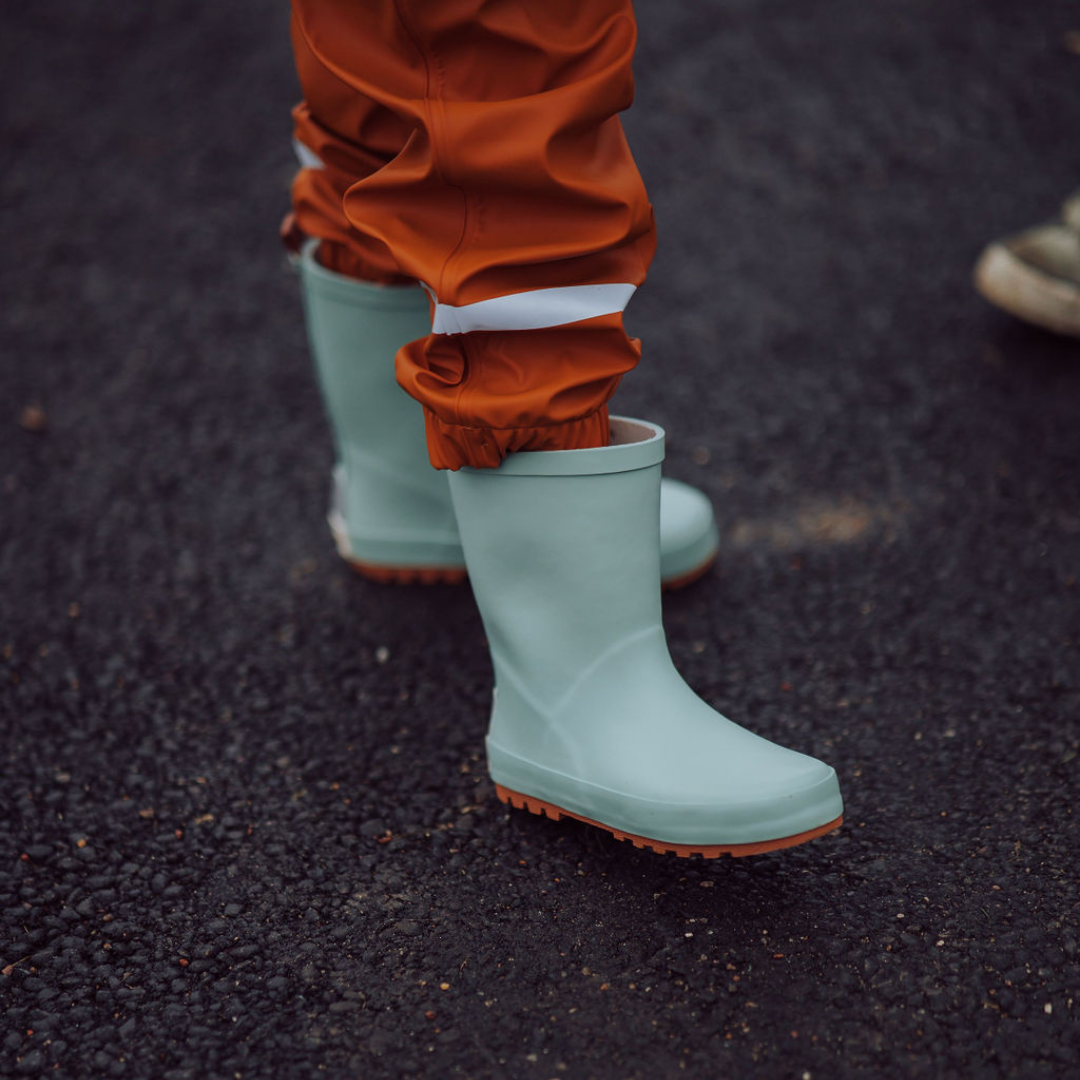 Green rubber boots worn with orange pants on a dark surface