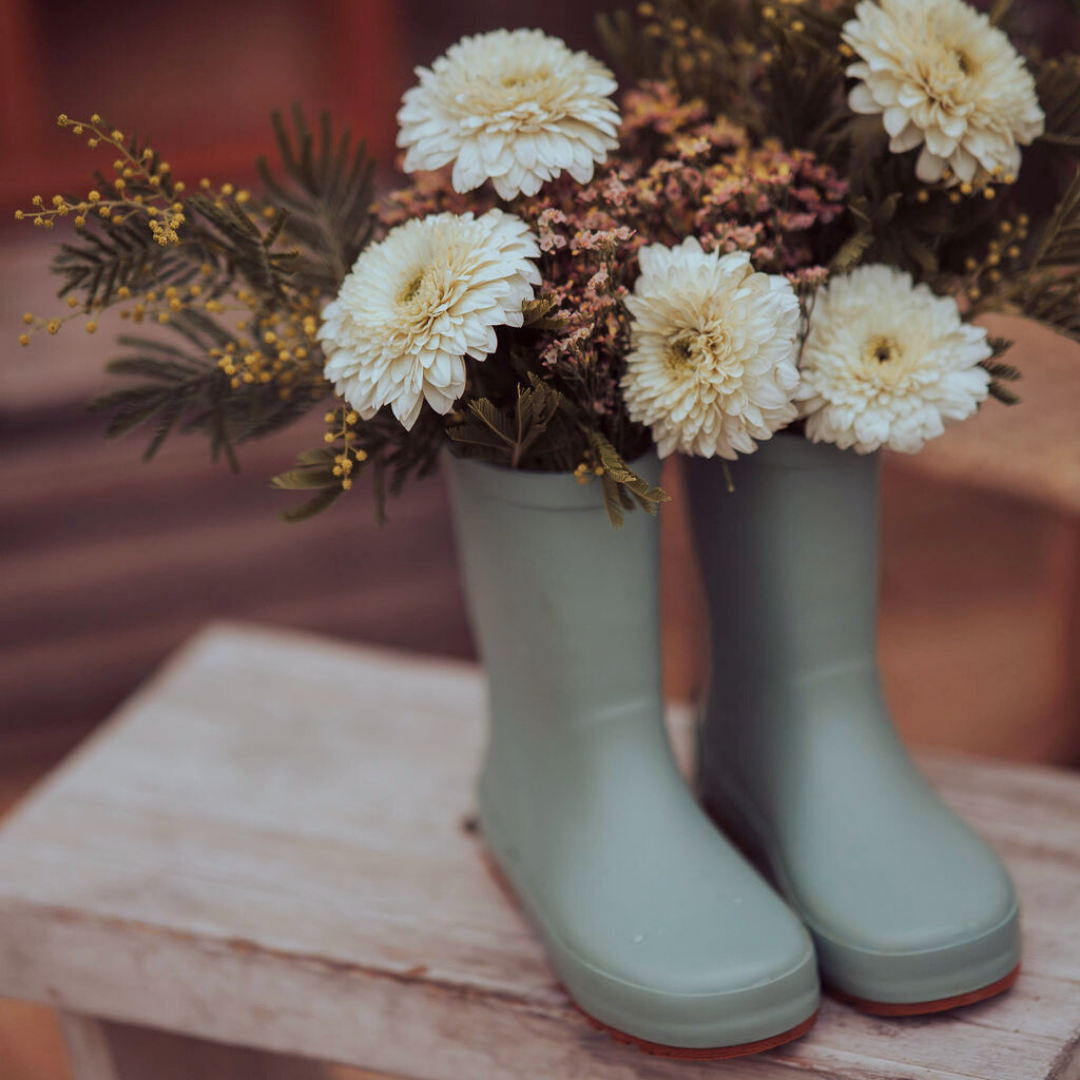 Green rubber boots with a floral arrangement on a wooden surface