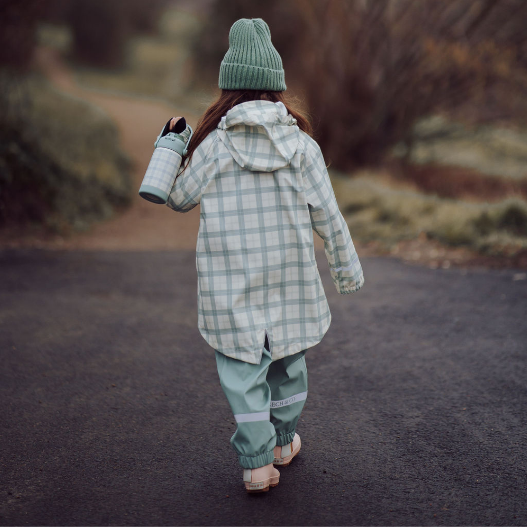 Person wearing a green plaid outfit walking on a path with a blurred natural background