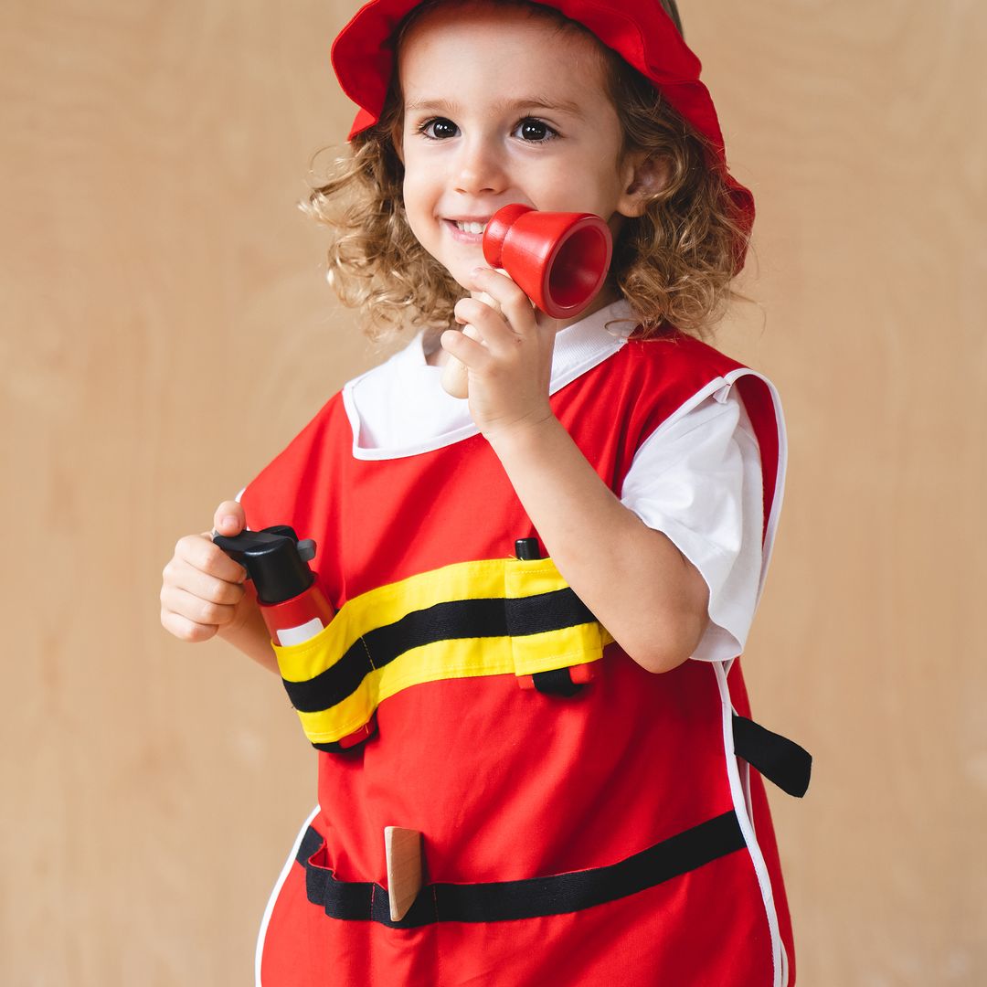 Child in a firefighter costume holding a toy megaphone against a beige background
