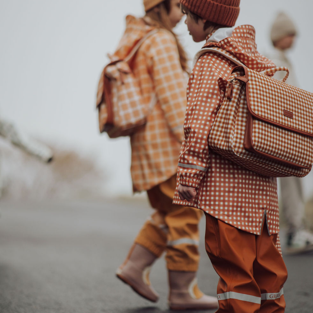 Two children in matching checkered outfits with backpacks walking outdoors.