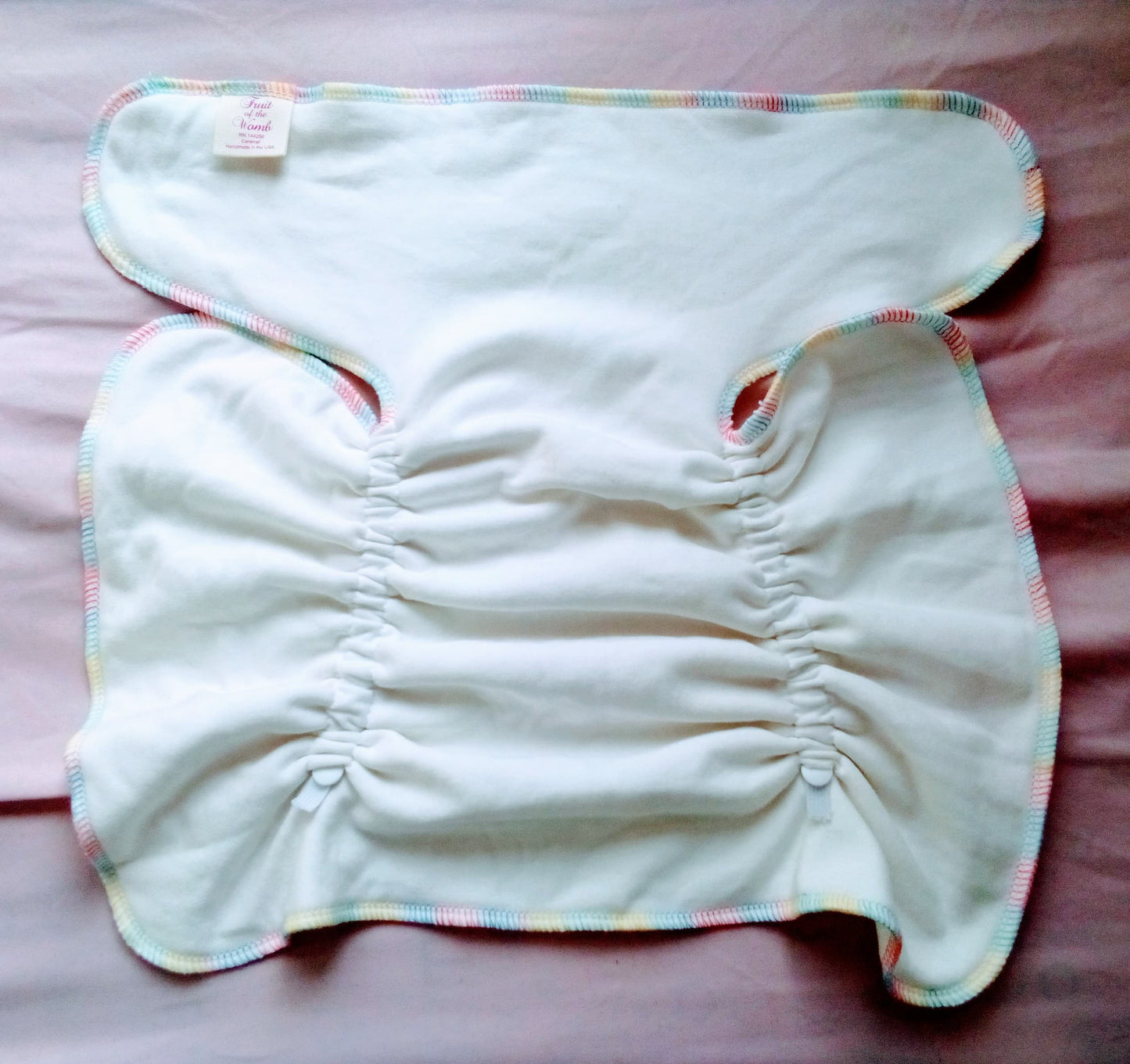 White baby diaper with colorful trim on a pink surface