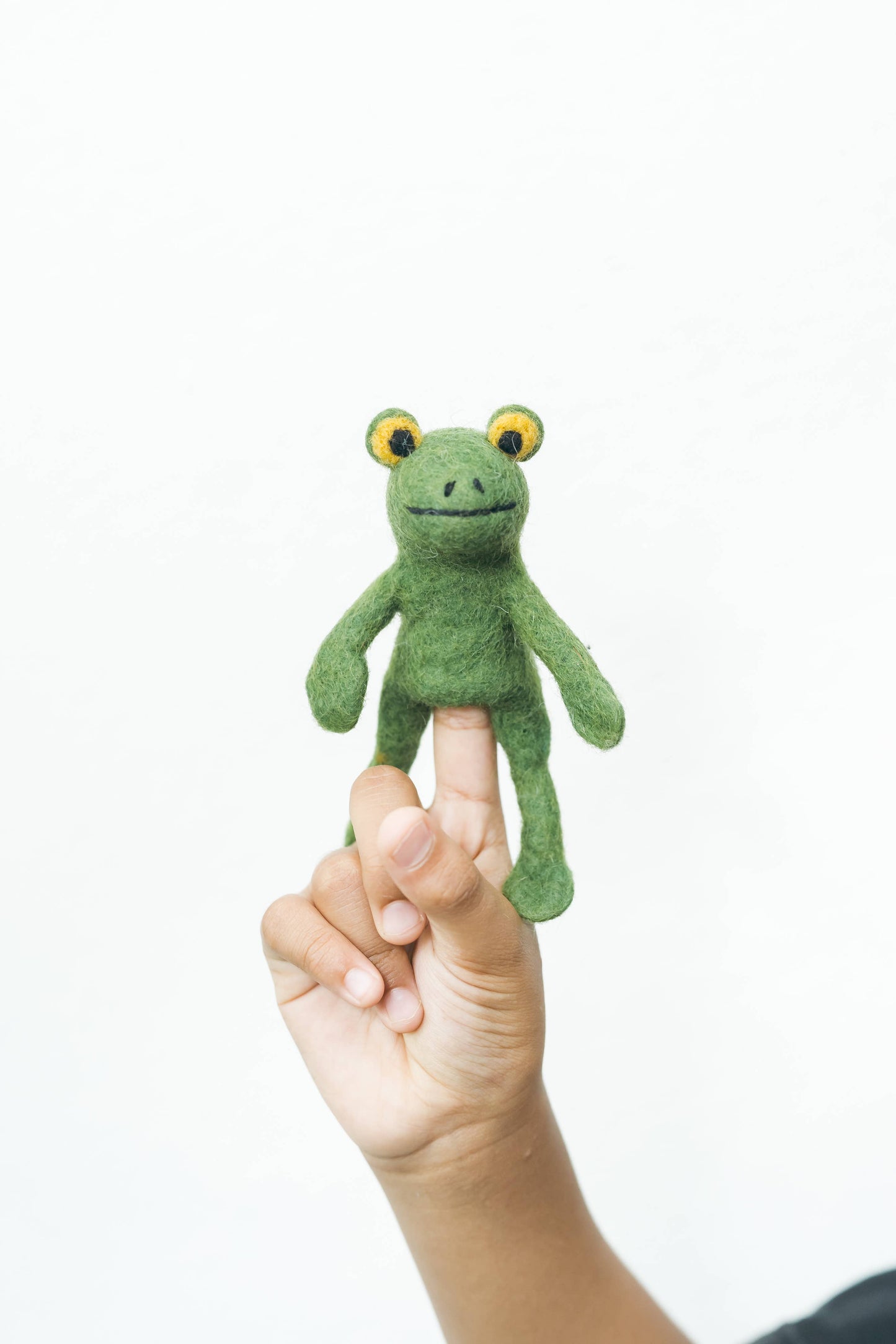 Green frog finger puppet on a person's finger against a white background