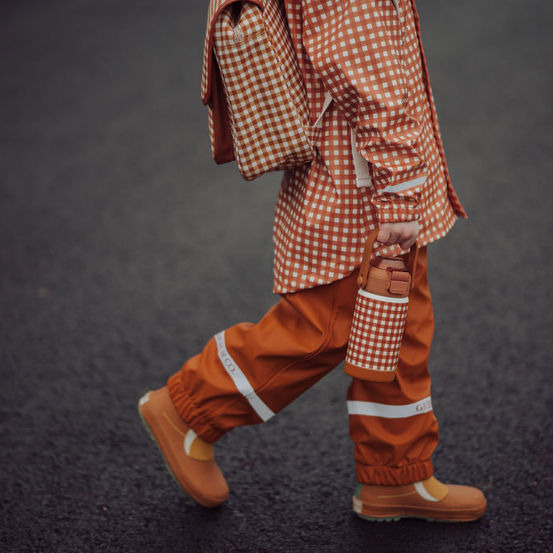 Person wearing a red and white checkered raincoat and pants with orange boots on a dark background
