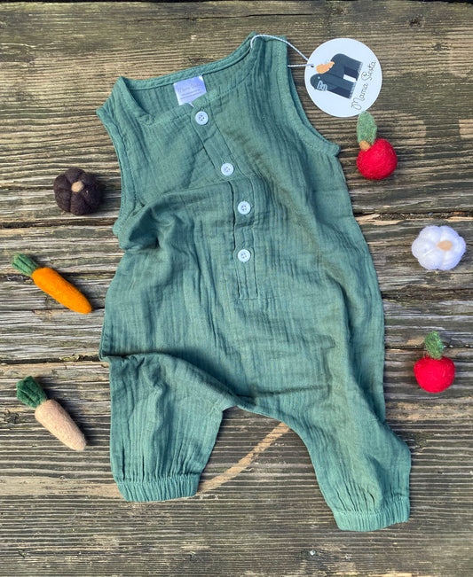 Green baby romper on a wooden surface with toy vegetables and flowers.