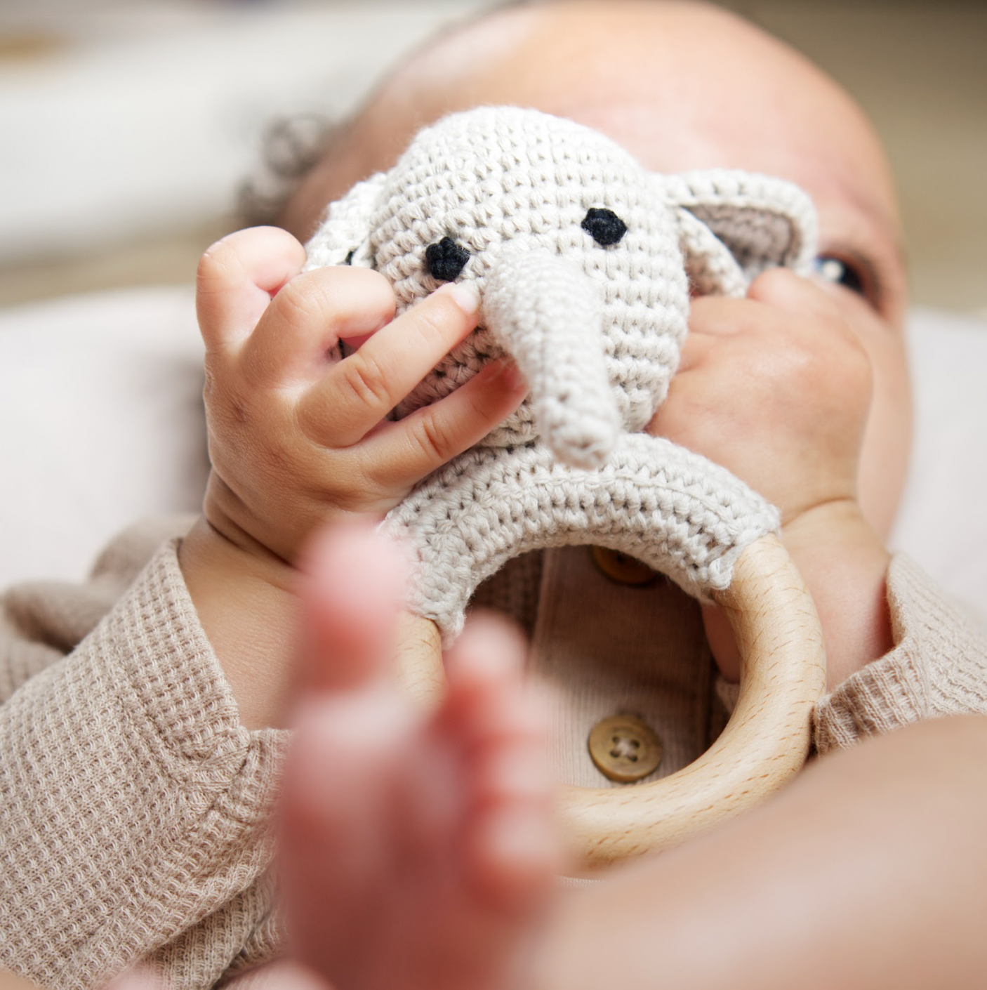 Baby holding a crocheted teething ring with a wooden base