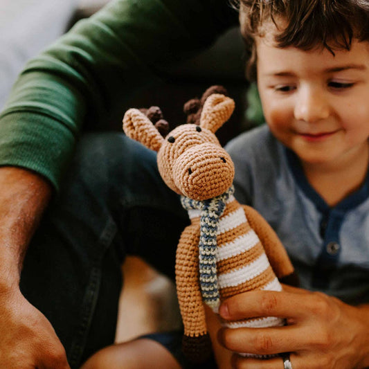 Child holding a crocheted giraffe toy with a striped scarf, sitting next to an adult.