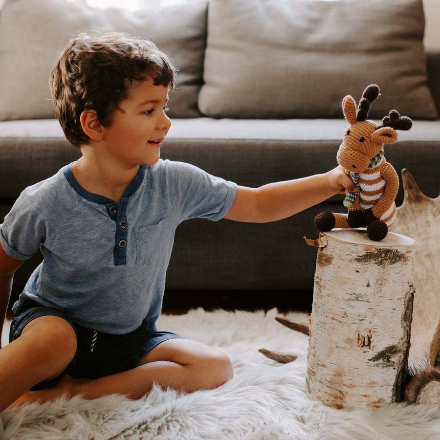 Child playing with a stuffed reindeer toy on a log in a cozy living room.
