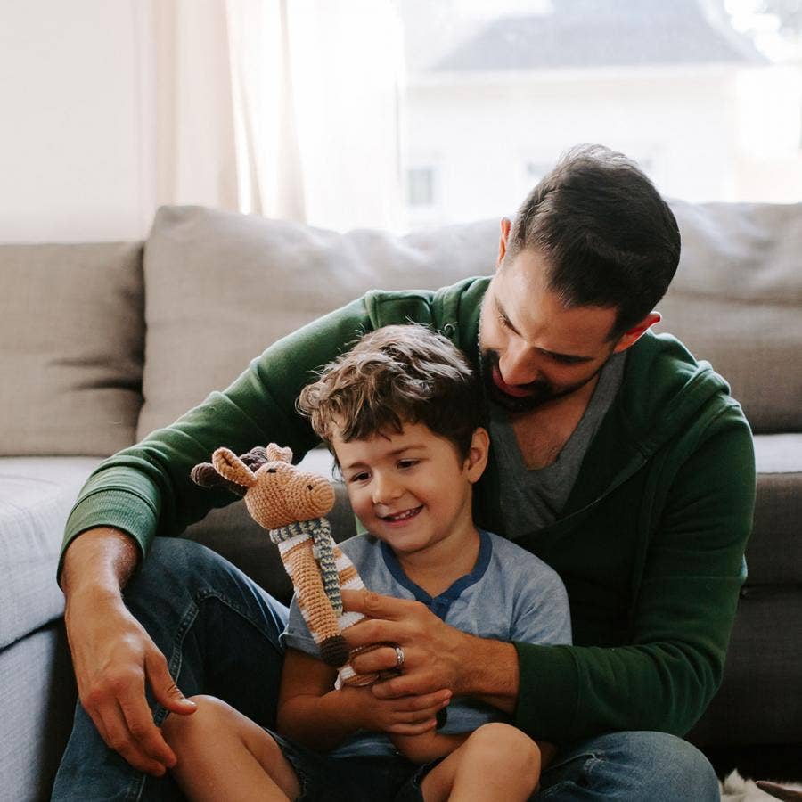 Man and child sitting on a couch with a toy, smiling indoors.