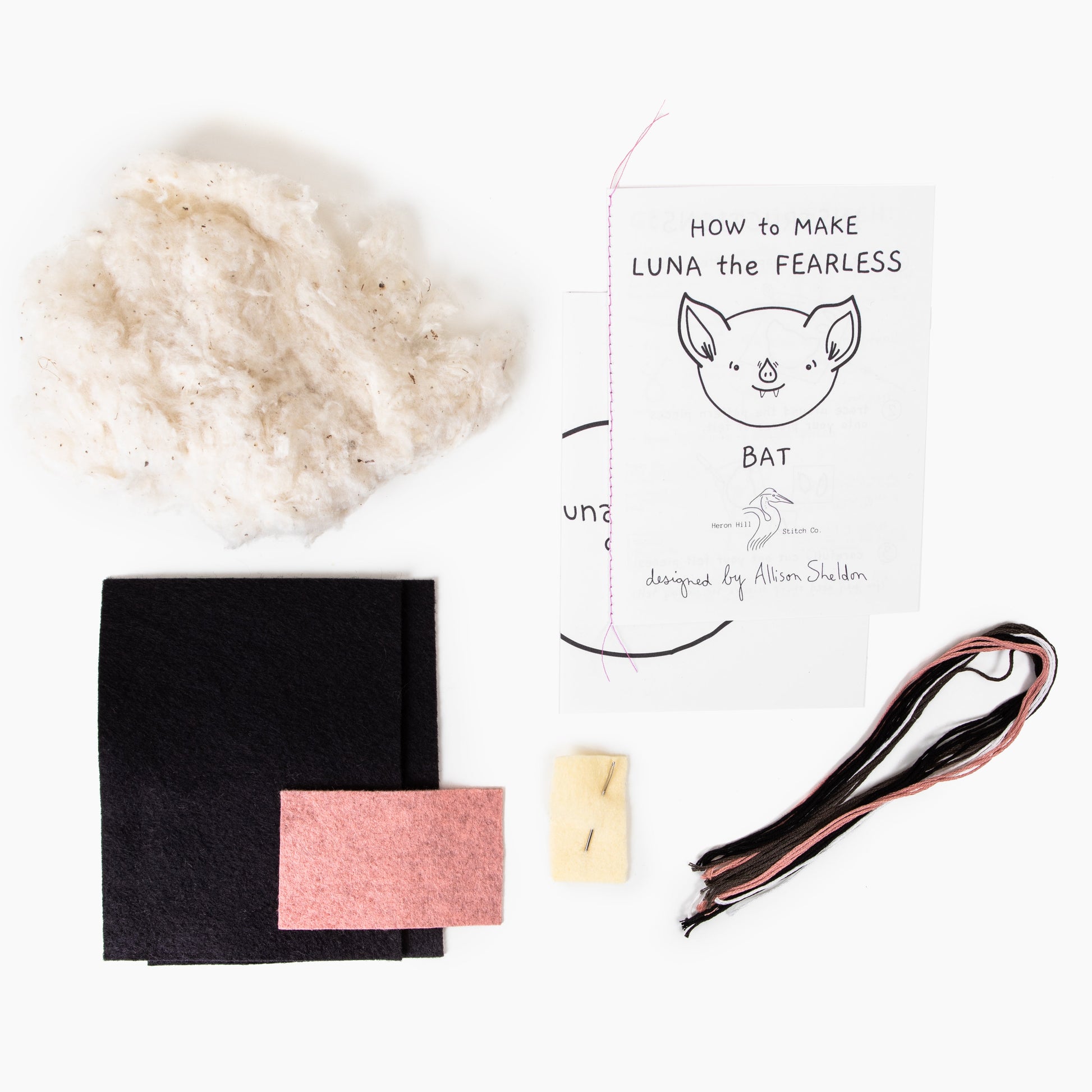 Crafting kit components including a black fabric square, pink card, white card with text, and a piece of ribbon on a white background.