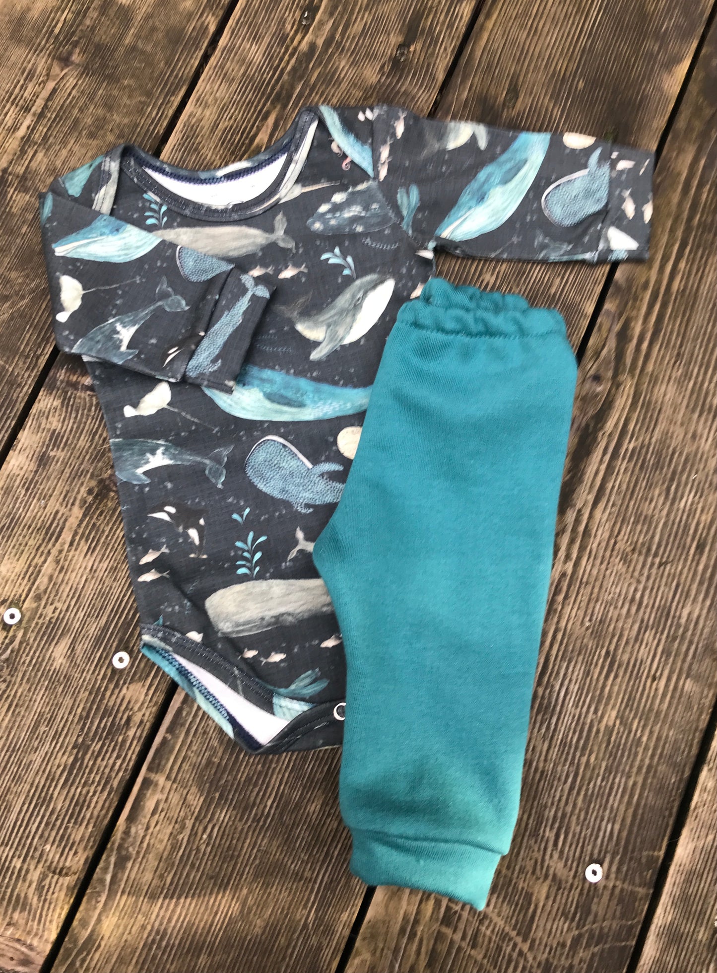 Baby outfit with whale pattern top and teal pants on a wooden surface
