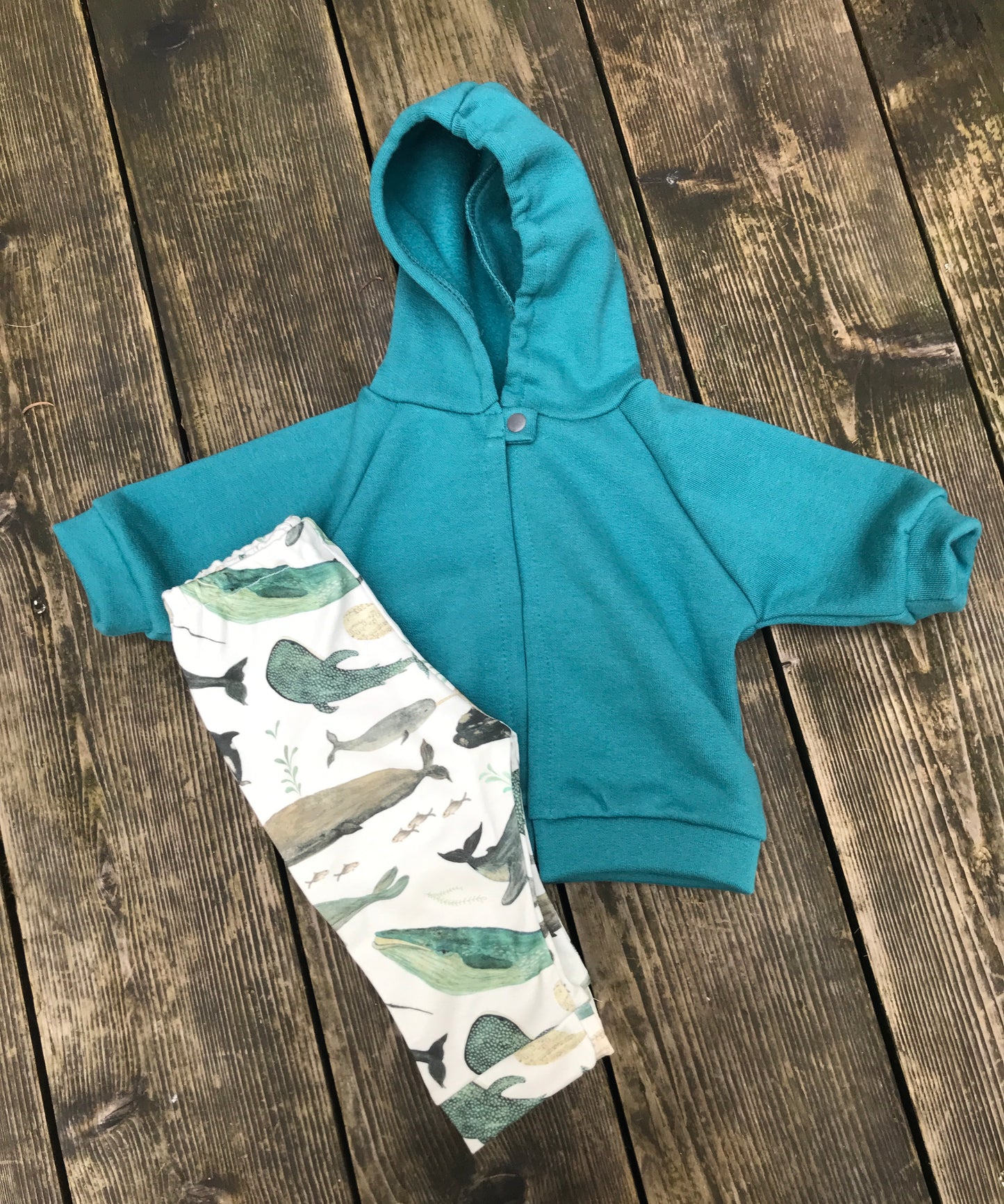 Teal hoodie and whale-patterned pants on a wooden surface