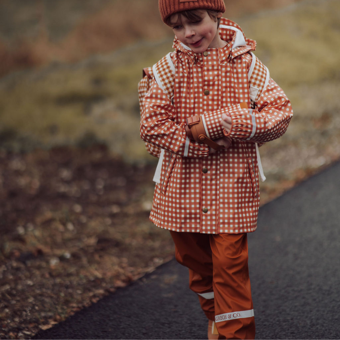Child wearing a red checkered raincoat and matching pants standing on a road.