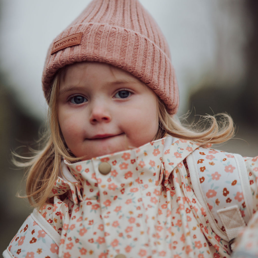 Child wearing a pink knit hat and floral coat outdoors