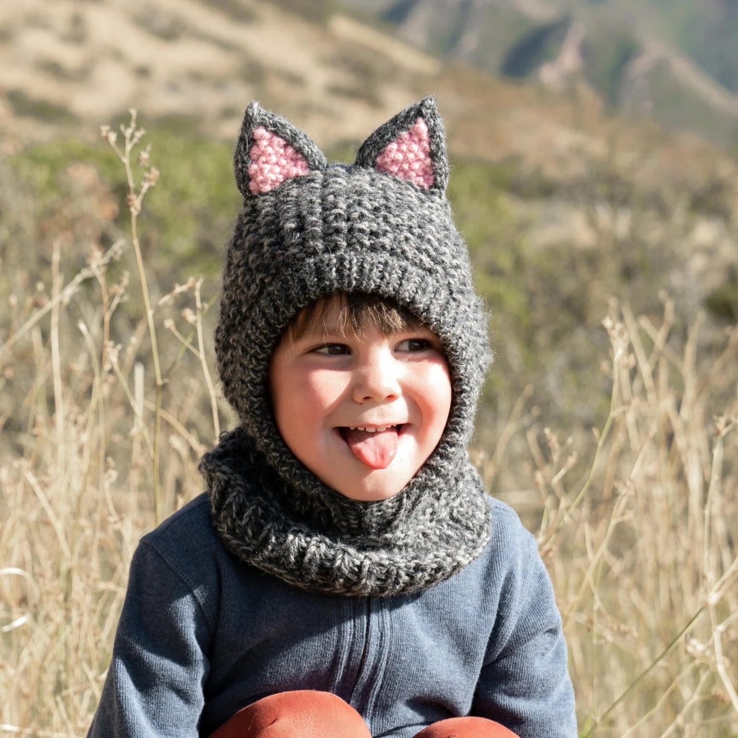 Child standing in a field wearing wool grey cat animal hood