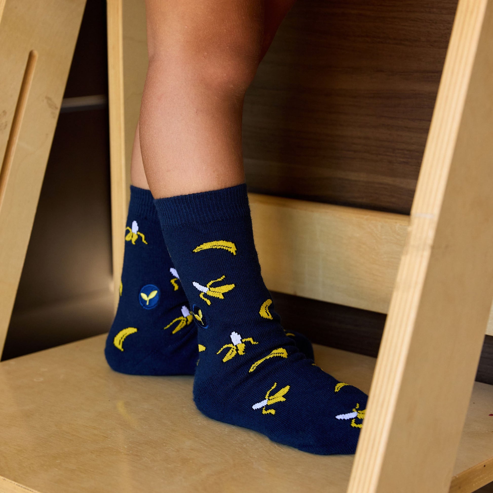 Person wearing blue socks with banana pattern on a wooden floor.