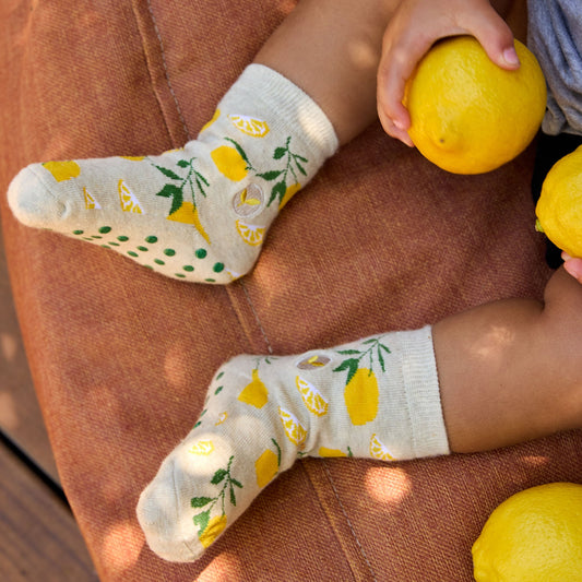 Child's feet wearing socks with lemon pattern holding lemons on brown surface