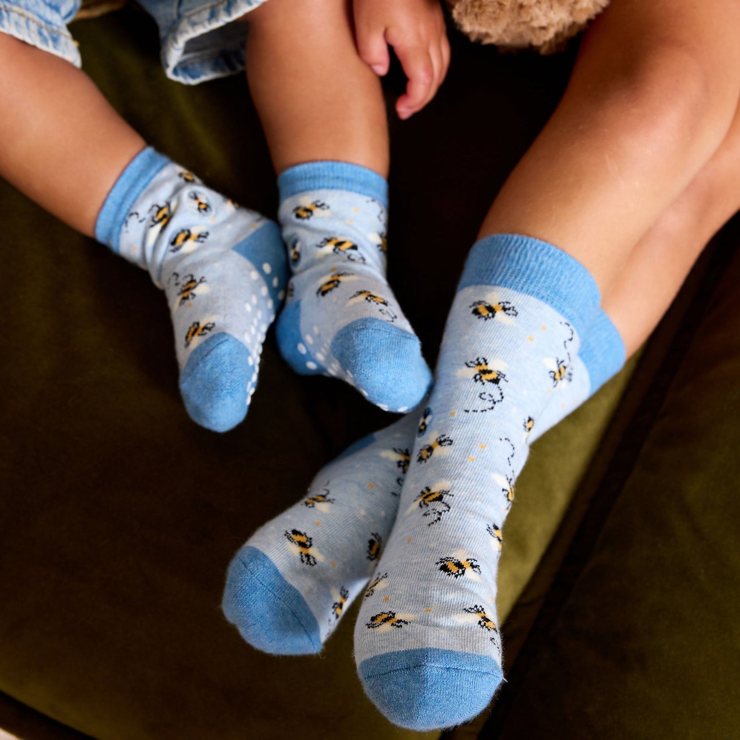 Two pairs of socks with bee pattern worn by children on a dark surface