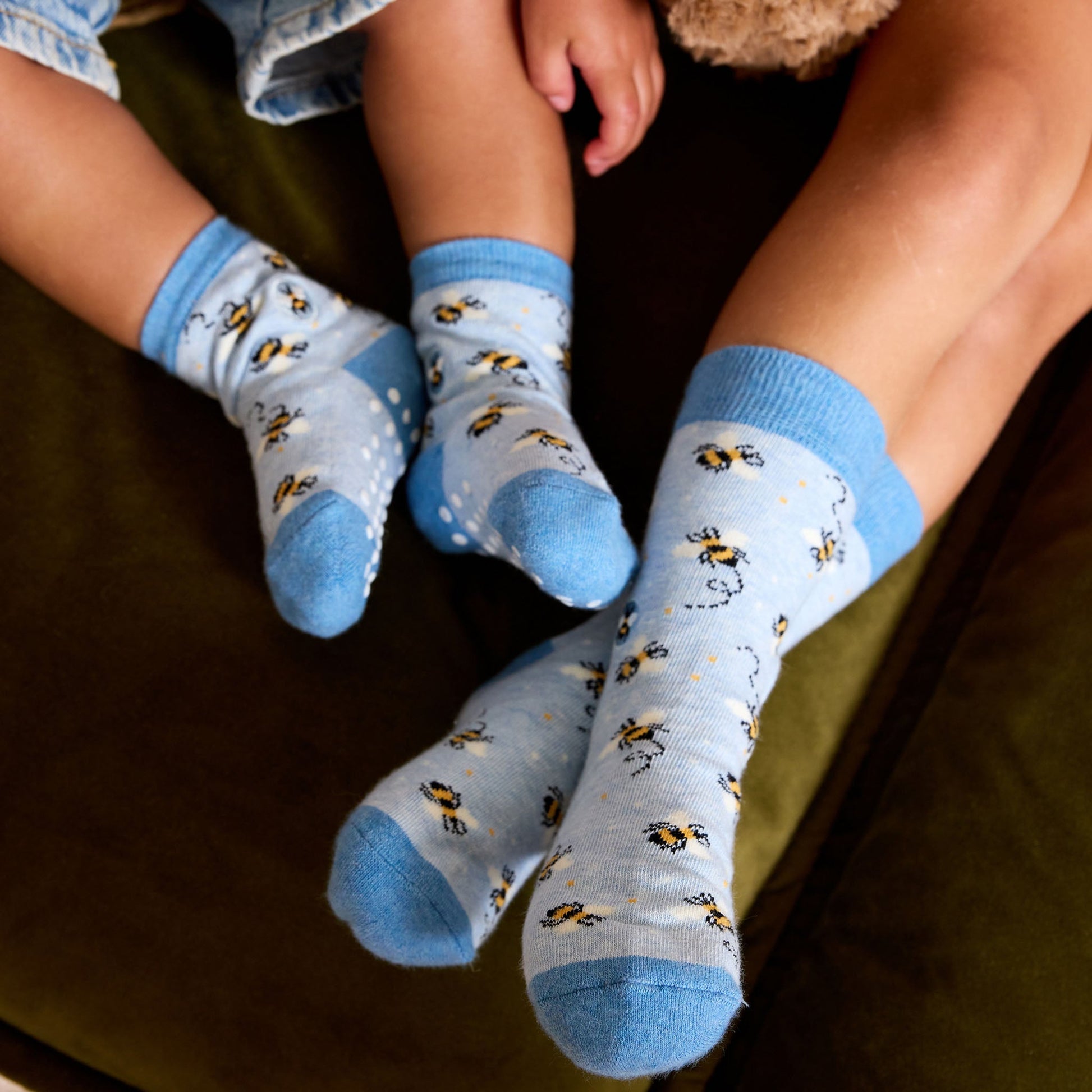 Two pairs of socks with bee pattern worn by children on a dark surface